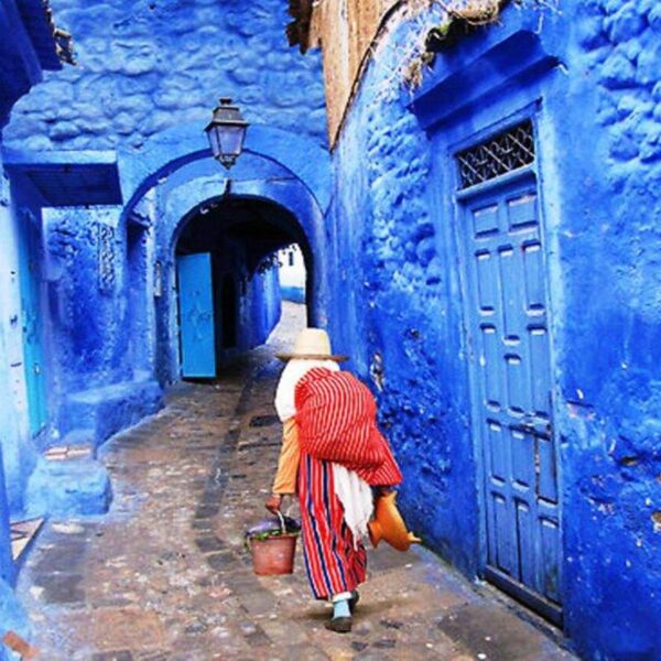 A Moroccan woman walking in the blue streets of Chefchaouen with our day trip from Fes.