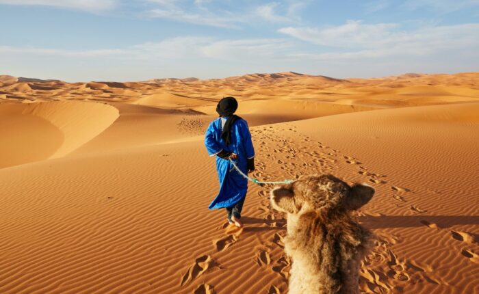 Uomo del deserto che guida un cammello nel deserto di Merzouga durante il nostro tour di 2 giorni da Errachidia.