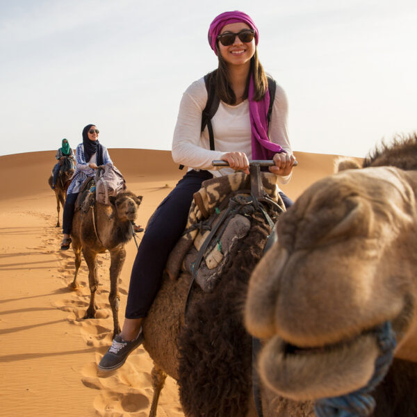 Una viaggiatrice con il sorriso che cavalca cammelli con i suoi amici nel deserto di Merzouga.