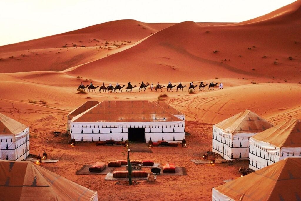 Luxury desert camp in Merzouga compared to Zagora: Camel ride in background