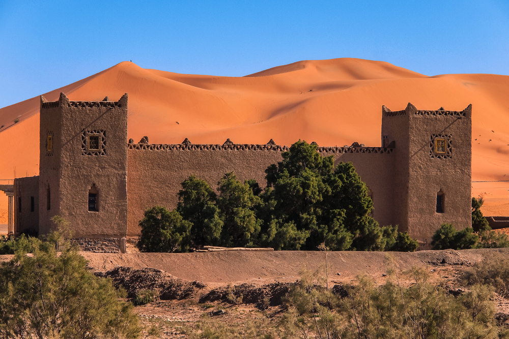 Casa construida con barro en el desierto de Merzouga, dunas de arena al fondo