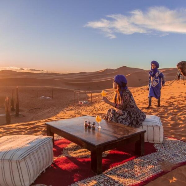 A solo female traveler sitting in Merzouga desert camp drinking orange juice.