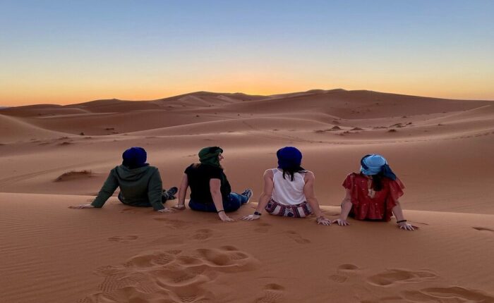 4 chicas contemplan la puesta de sol en el desierto de Merzouga durante el viaje de 8 días desde Tánger.