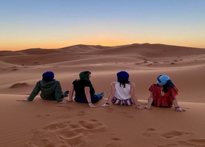 4 chicas contemplan la puesta de sol en el desierto de Merzouga durante el viaje de 8 días desde Tánger.