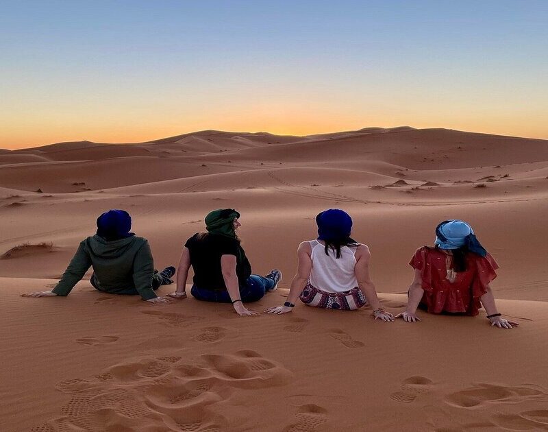 4 chicas contemplan la puesta de sol en el desierto de Merzouga durante el viaje de 8 días desde Tánger.