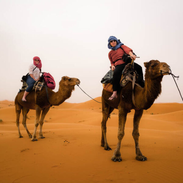 Two travelers riding camels in the Sahara desert of Merzouga during our 4-day tour from Tangier.