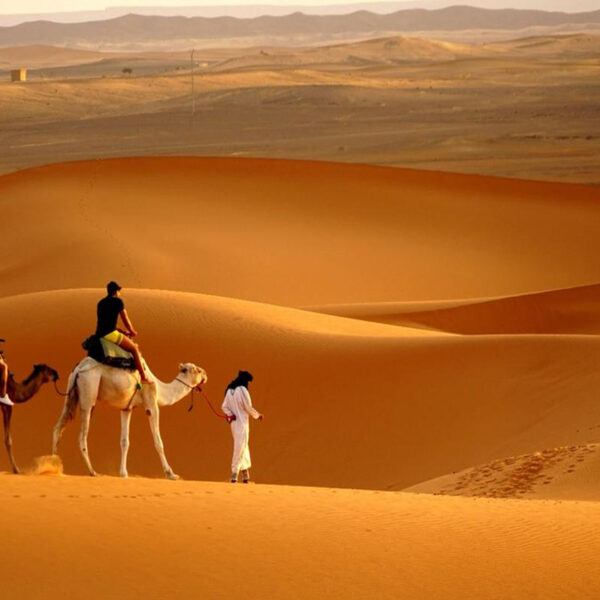 Two tourists riding camels with their camel driver in Merzouga with our 5-day trip from Tetouan to Marrakech.