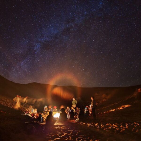 Turistas alrededor de la hoguera en el desierto por la noche durante el viaje de 4 días por Marruecos de Marrakech a Tánger.