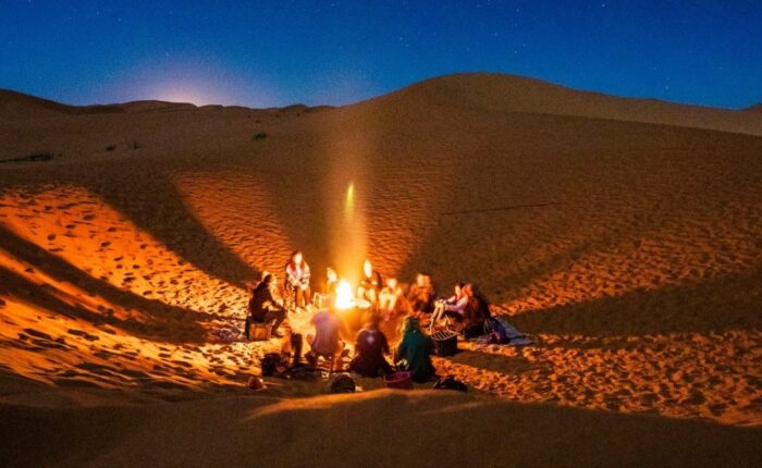 Viaggiatori intorno al fuoco del campo di Merzouga durante il tour di 4 giorni da Ouarzazate a Fes.