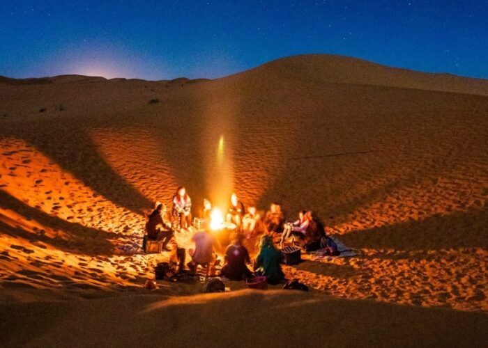 Viaggiatori intorno al fuoco del campo di Merzouga durante il tour di 4 giorni da Ouarzazate a Fes.