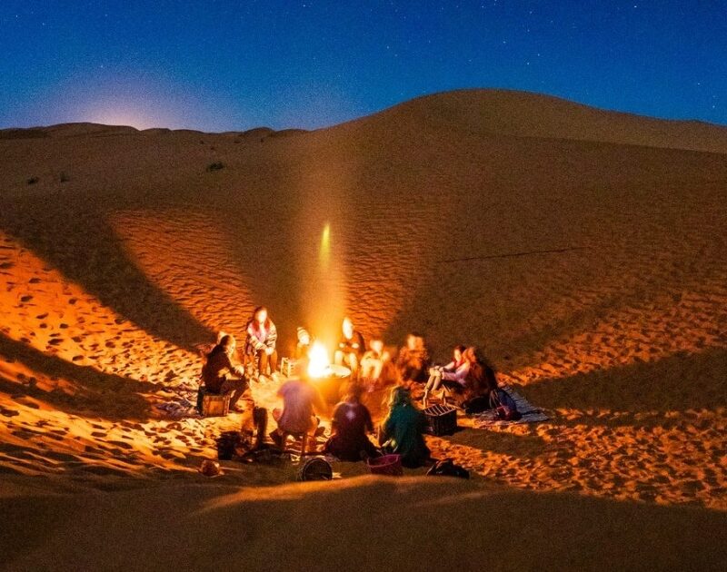 Viaggiatori intorno al fuoco del campo di Merzouga durante il tour di 4 giorni da Ouarzazate a Fes.