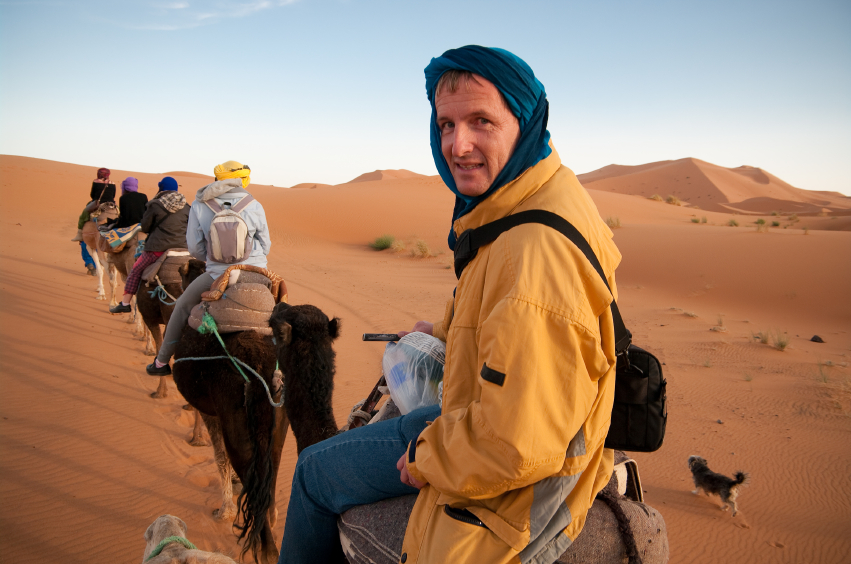 A tourist in the Sahara desert riding a camel with a smile on his face