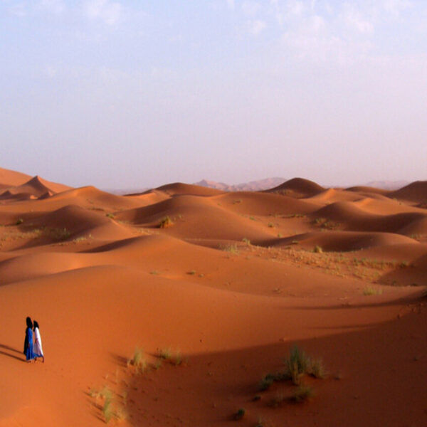 Two people walking in the Merzouga desert with our 12-day tour from Marrakech.