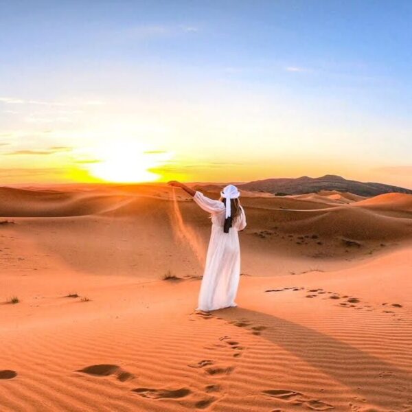 Una mujer vierte arena durante la puesta de sol en el desierto.