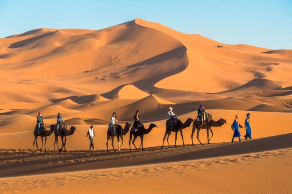 Persone a cavallo di cammelli nel deserto del Sahara di Merzouga che si chiedono quanti giorni trascorrere in Marocco.